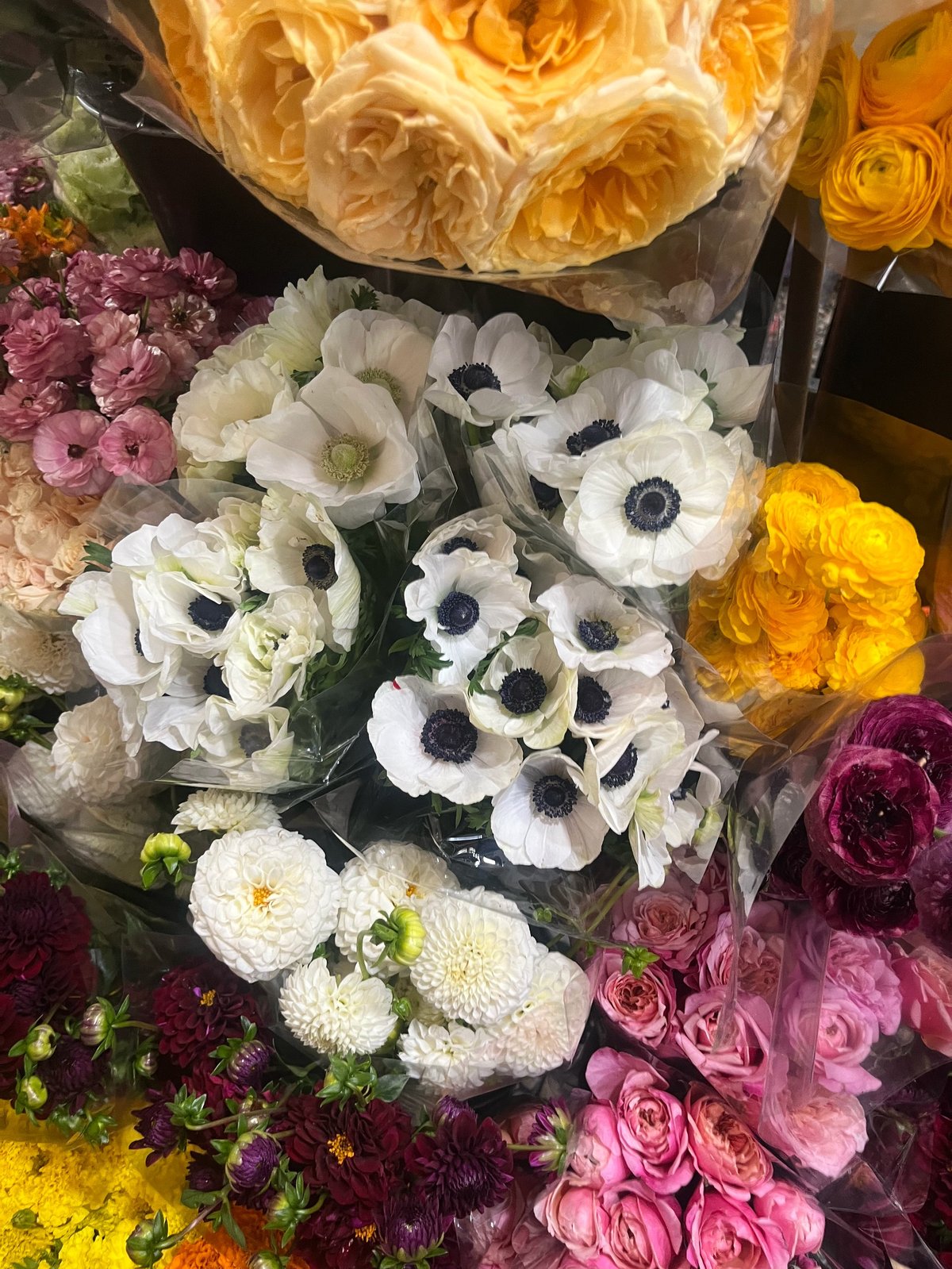 Colorful flower bouquets display featuring white anemones, yellow roses, pink peonies, and burgundy blooms at a florist shop