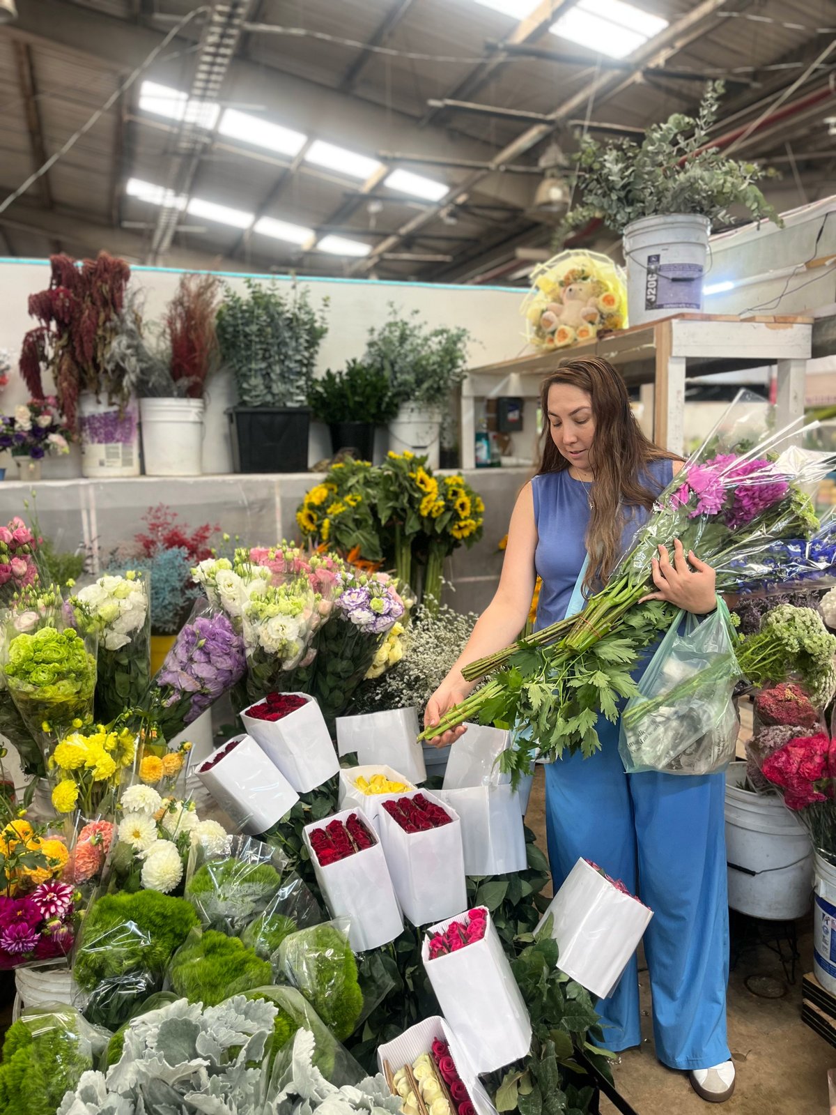 Woman florist arranging fresh flowers in a warehouse flower shop surrounded by colorful blooms and floral arrangements
