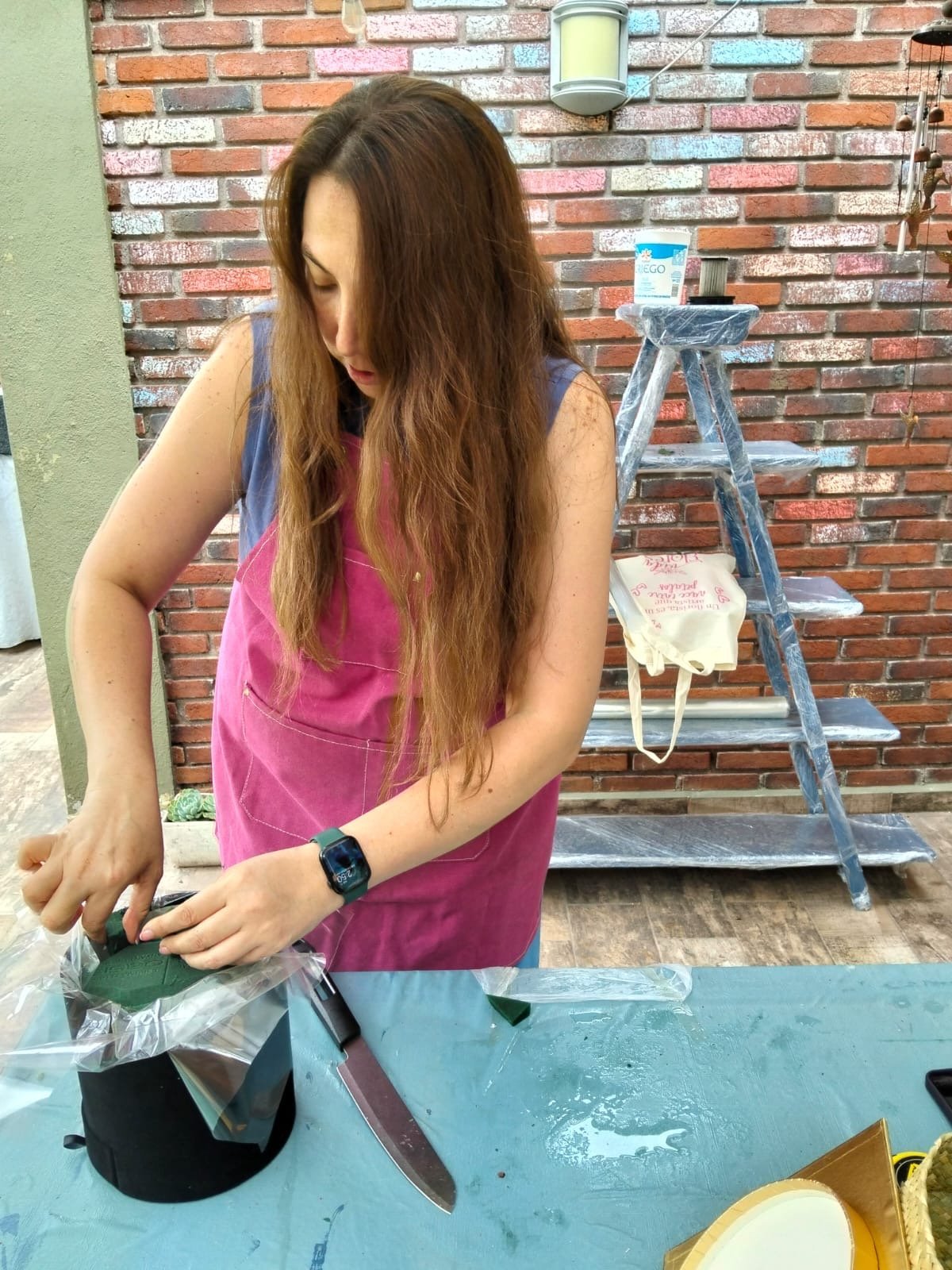 Woman in pink tank top painting a surface with a brush during a home renovation project against a brick wall