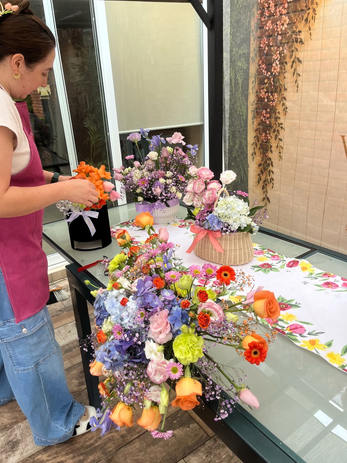 Woman arranging colorful fresh flowers including roses, gerberas, and hydrangeas on a display table indoors