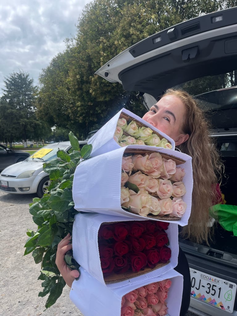 Woman holding multiple bouquets of wrapped flowers in various colors including white, peach, red, and coral by a car trunk