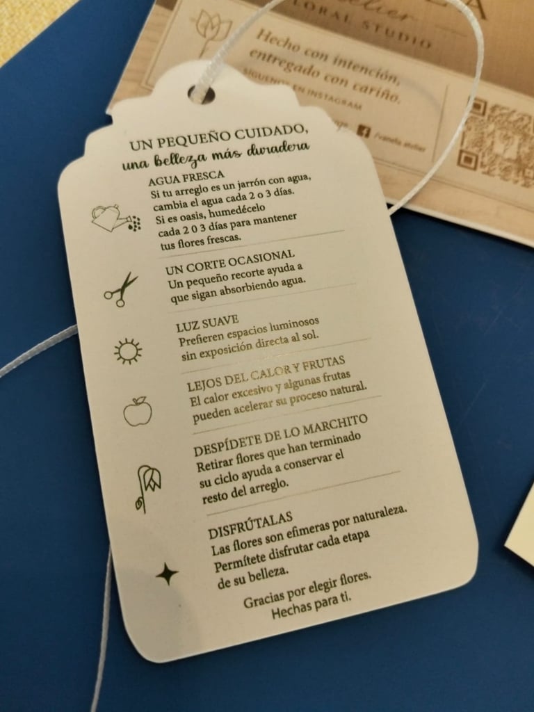 Spanish care instruction tag for flowers with watering and maintenance tips, displayed with string on blue background