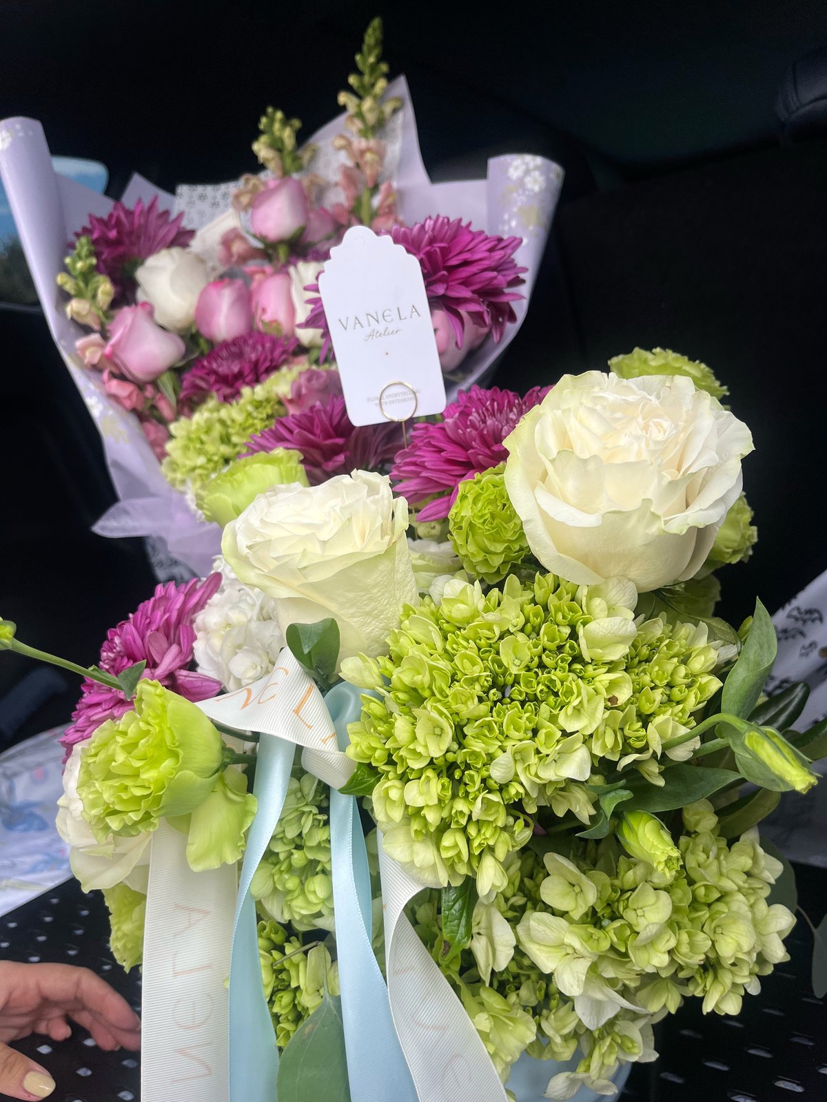 Two bouquets of fresh flowers featuring white roses, lime green hydrangeas, magenta dahlias, and white carnations with blue ribbon and Vanda label