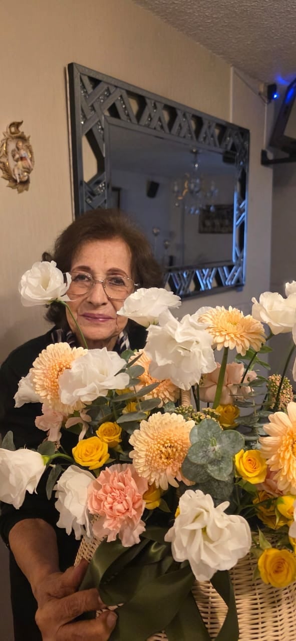 Woman wearing glasses smiling while holding a large bouquet of white, pink, and yellow flowers in a wicker basket