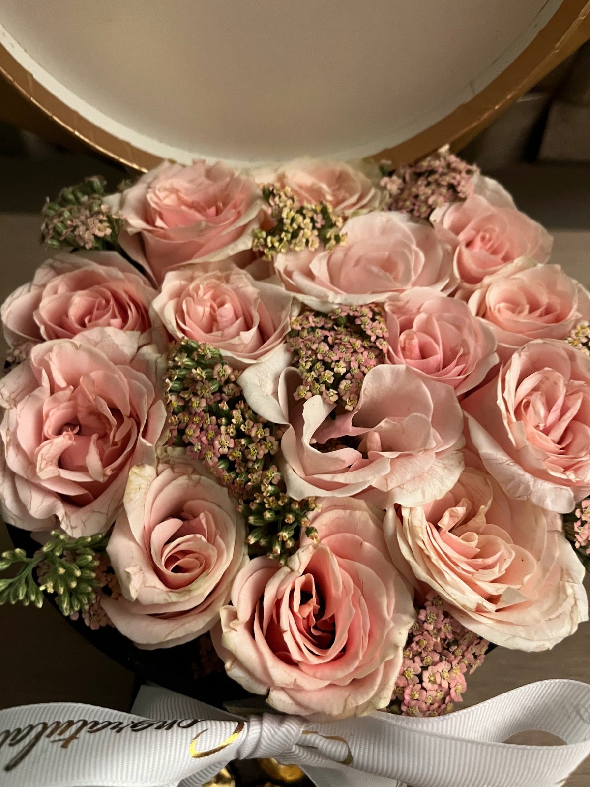 Overhead view of a luxurious floral arrangement in a white hat box with pink roses, dried babys breath, and greenery accents