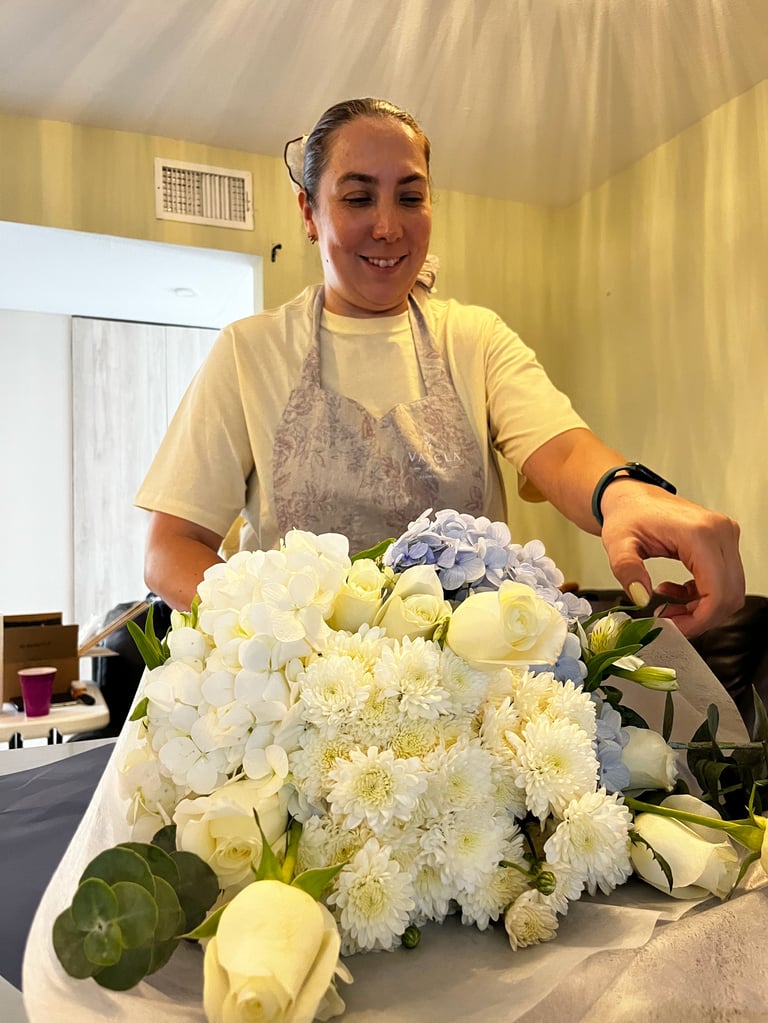 Woman arranging white and blue flowers in a yellow kitchen, smiling while working with hydrangeas and roses