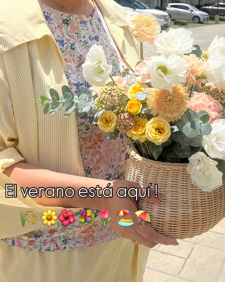 Person holding a wicker basket filled with vibrant summer flowers including yellow roses, white peonies, and green eucalyptus