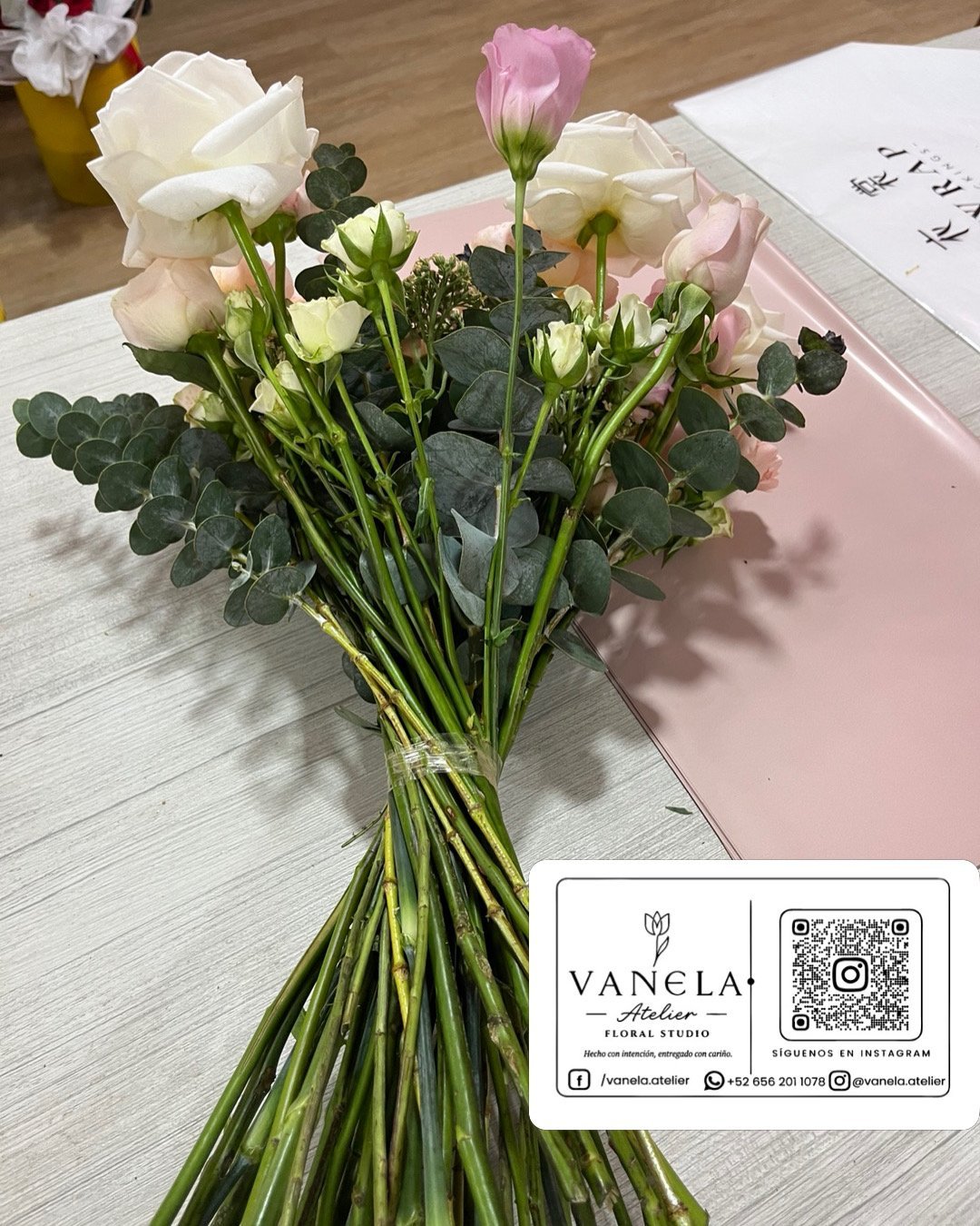 Glass vase with white and pink flowers and eucalyptus stems next to a Vanela Atelier florist business card