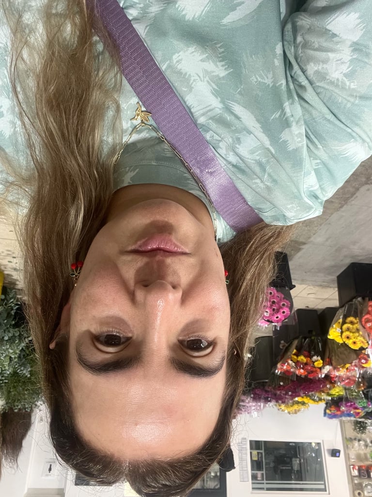 Selfie of person with long brown hair wearing purple headband, shot upside down with flowers visible in background