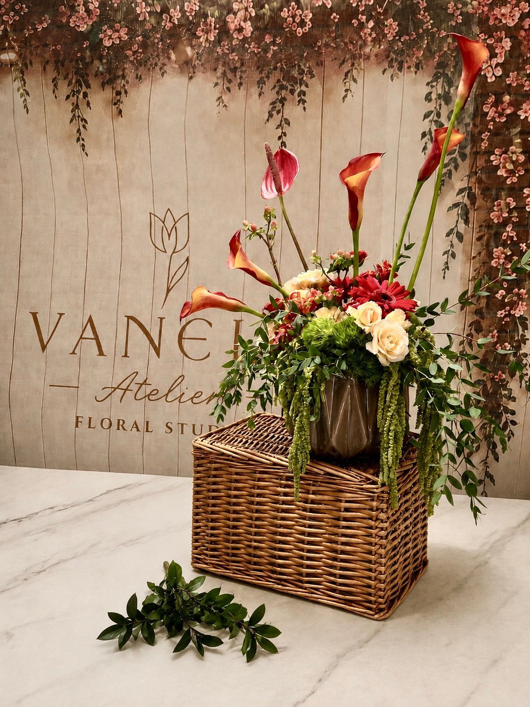 Luxurious floral arrangement in woven basket with red calla lilies, white roses, and cascading greenery on marble table