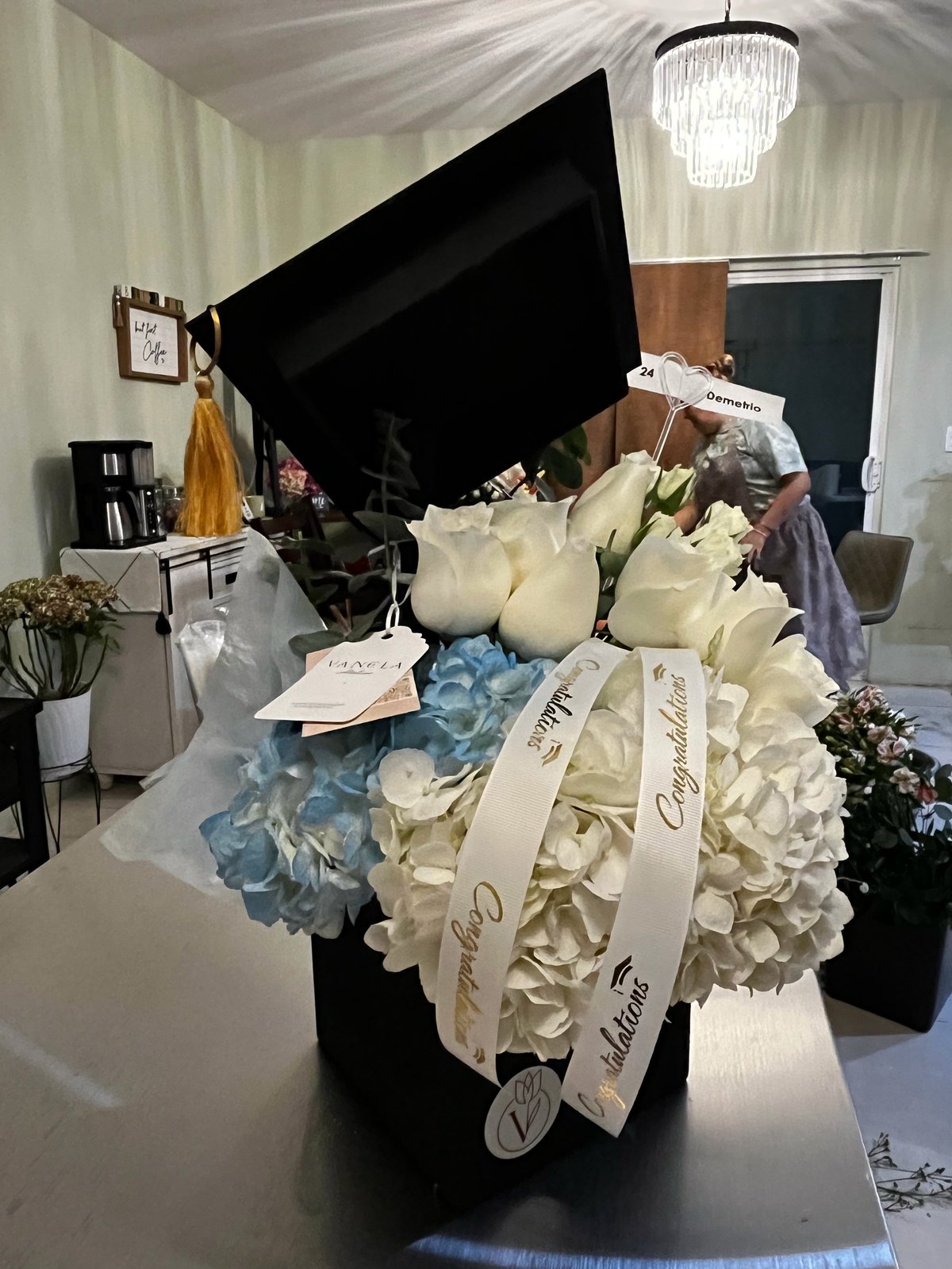 Elegant floral arrangement with white and blue flowers in a black piano-shaped planter displayed on a white table in a modern event space