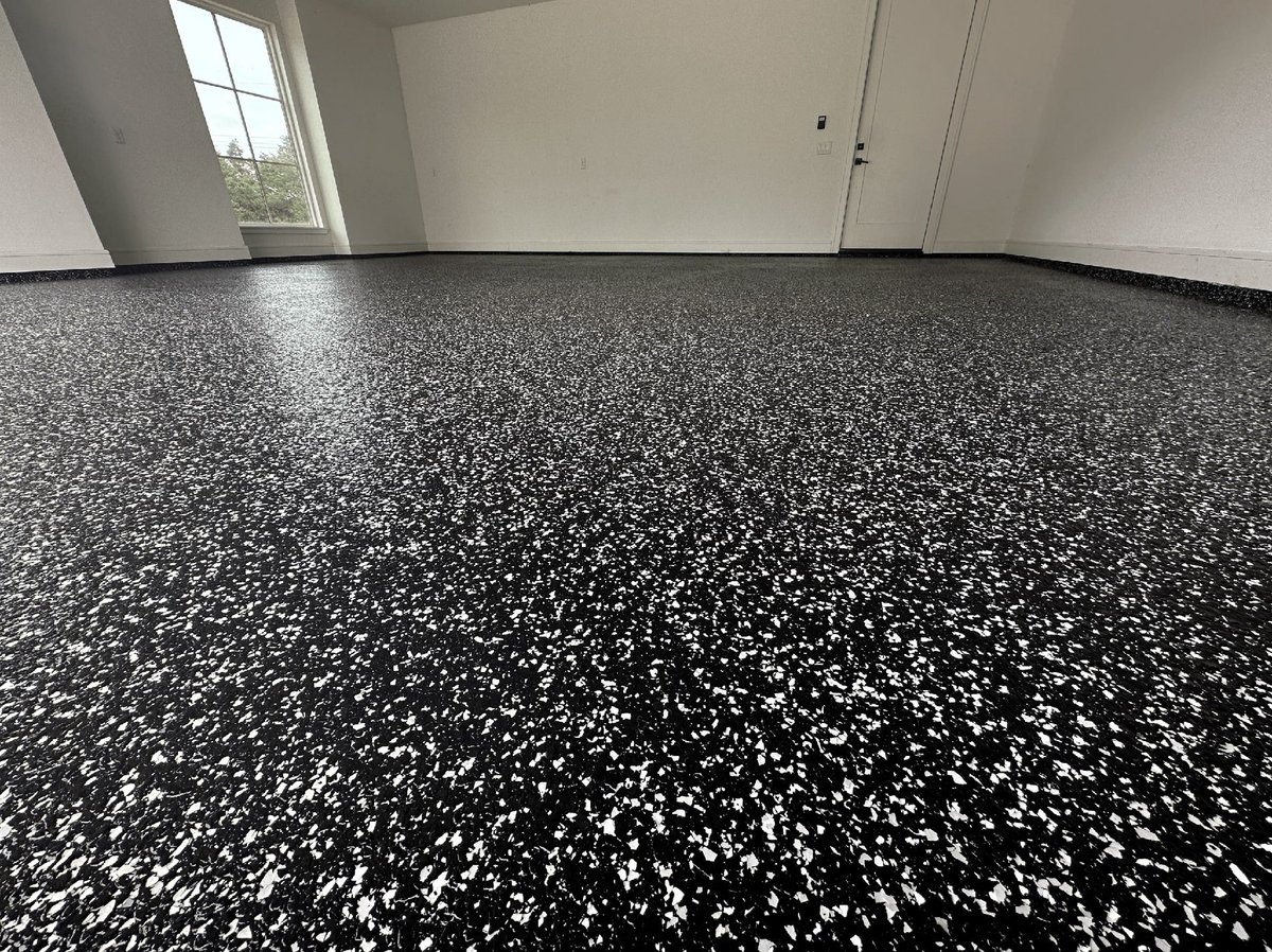 Empty room with black speckled epoxy flooring, white walls, window, and white door