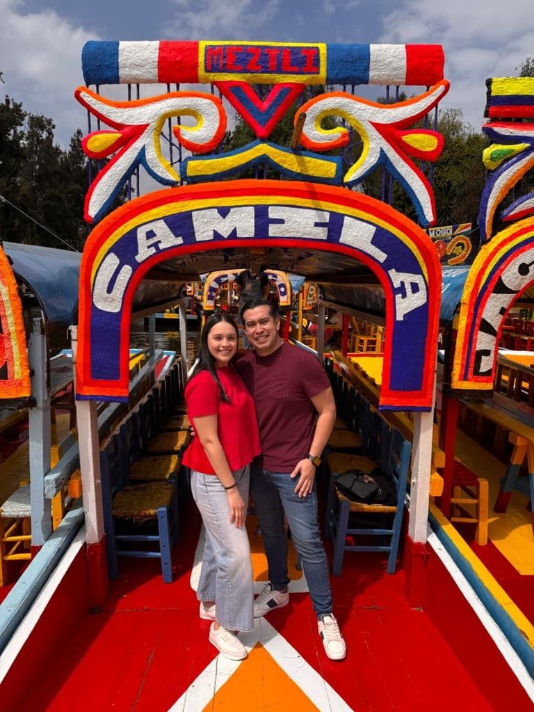 Pareja sonriendo dentro de una trajinera decorada en colores rojo, azul y amarillo con detalles ornamentales.
