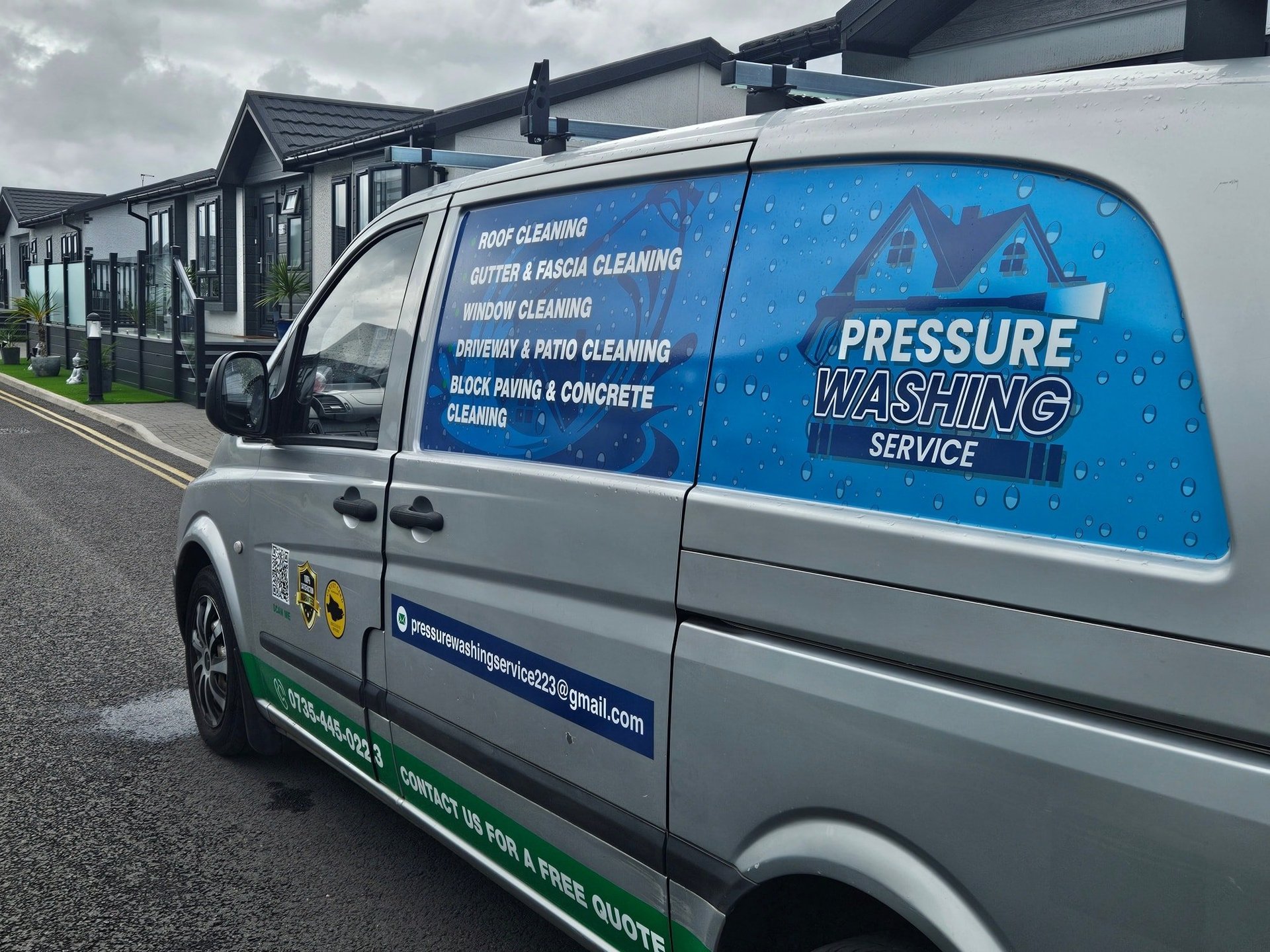 White van with blue graphics advertising pressure washing services, parked in driveway with houses visible in background