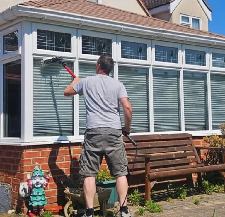 Man cleaning windows of a brick conservatory with white frames and green louvered panels