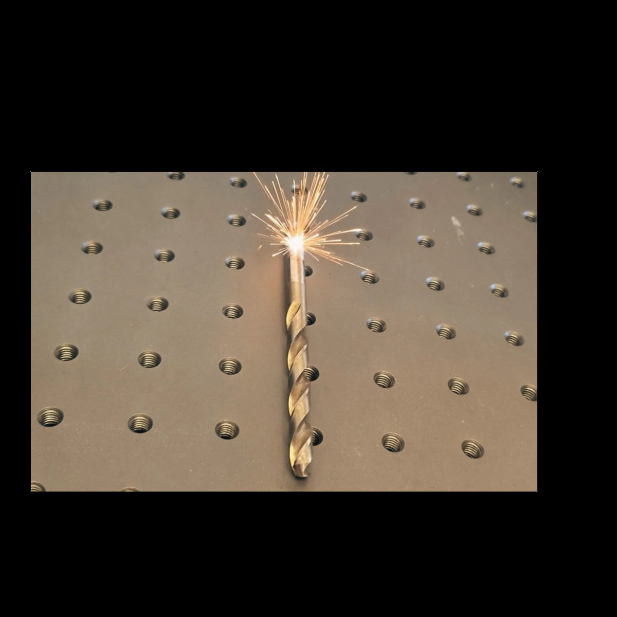 Gold twist drill bit with sharp tip spinning against pegboard with metal holes