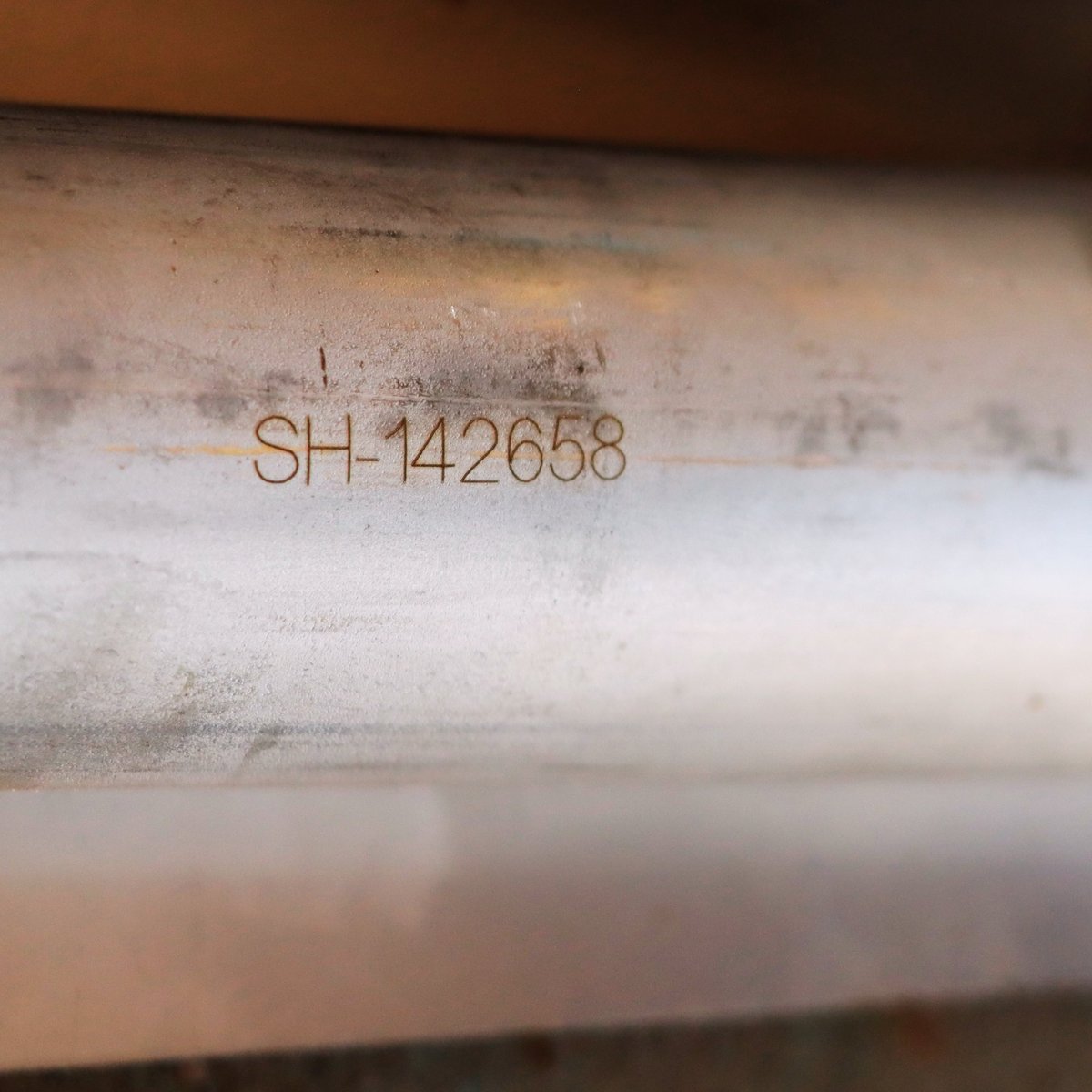Close-up of a metal pipe or tube with engraved identification code SH-142658 visible on its surface