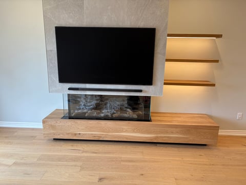 Modern living room with flat-screen TV mounted above a fireplace insert on wooden media console, with illuminated wall shelves