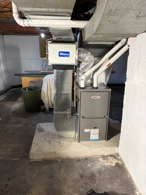 Furnace and HVAC system installed in a basement utility room with metal ductwork and thermostat mounted on wall above.