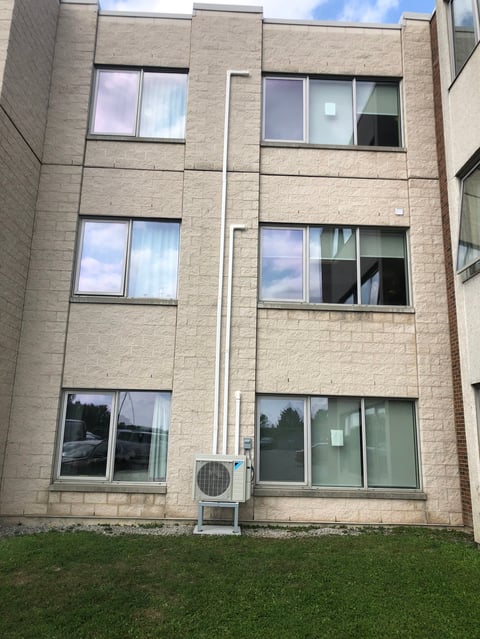 Tan brick apartment building with three floors of paired windows and a white downspout, set against green grass.