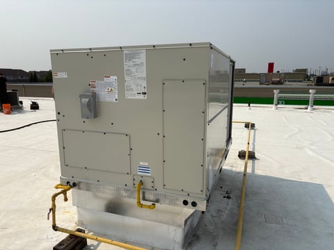 HVAC unit mounted on commercial rooftop with yellow support brackets and electrical connections visible