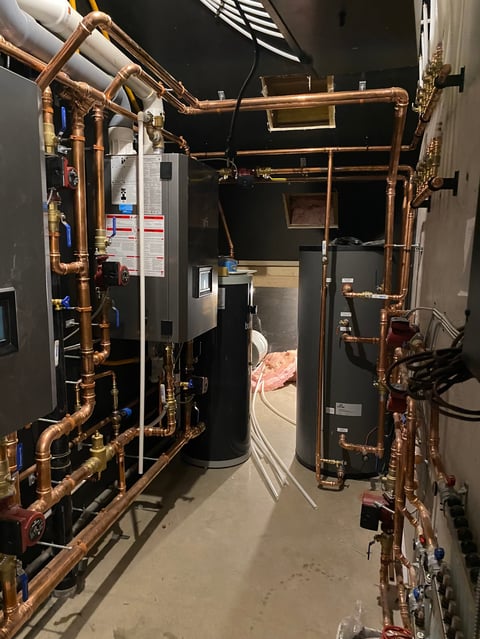 Complex plumbing and heating system with copper pipes, water heater, and connected equipment in a basement utility room.