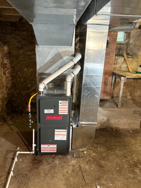 Goodman furnace with metal ductwork in basement corner, showing heating unit installation.