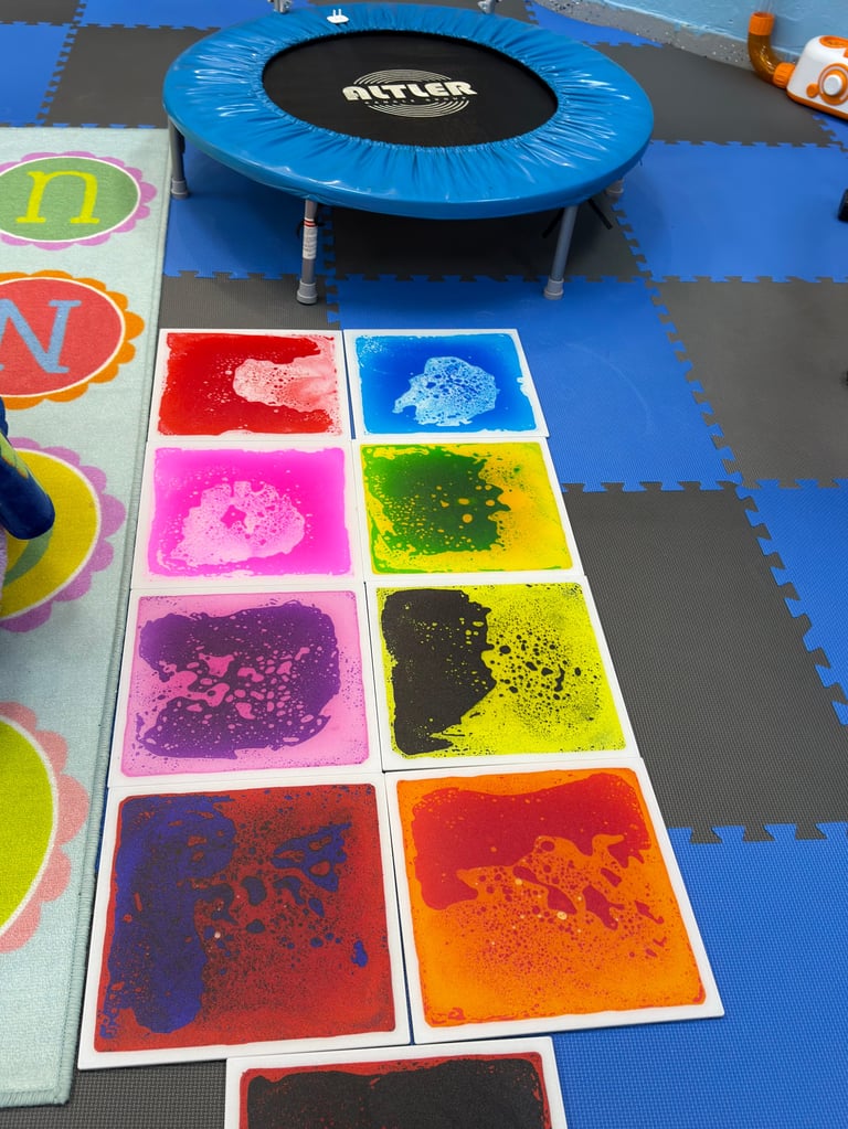 Blue trampoline and colorful sensory activity cards with paint splatter designs on a foam mat floor