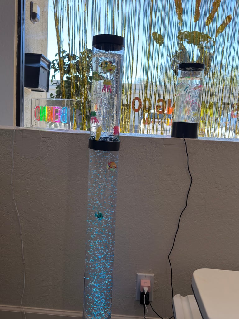 Tall glitter-filled tower aquarium with black caps mounted on wall near window with colorful text