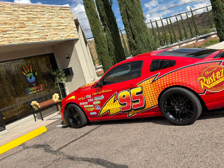 Red race car number 95 with yellow flame design parked on driveway in front of modern house