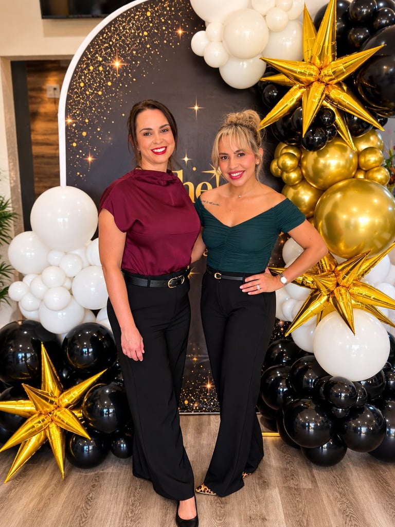 Two women posing in front of elegant New Years Eve decorations featuring black, white, and gold balloons and stars
