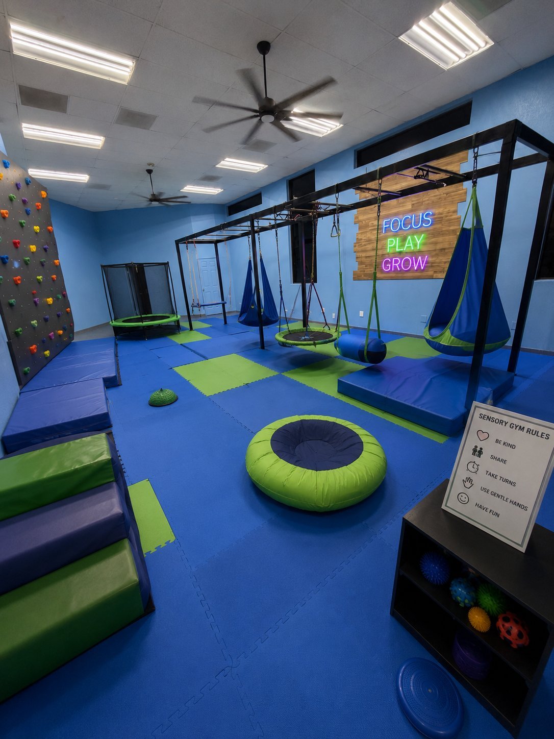 Modern indoor play gym with blue flooring, lime green accents, hanging swings, trampoline, climbing wall, and neon play-grow signage.