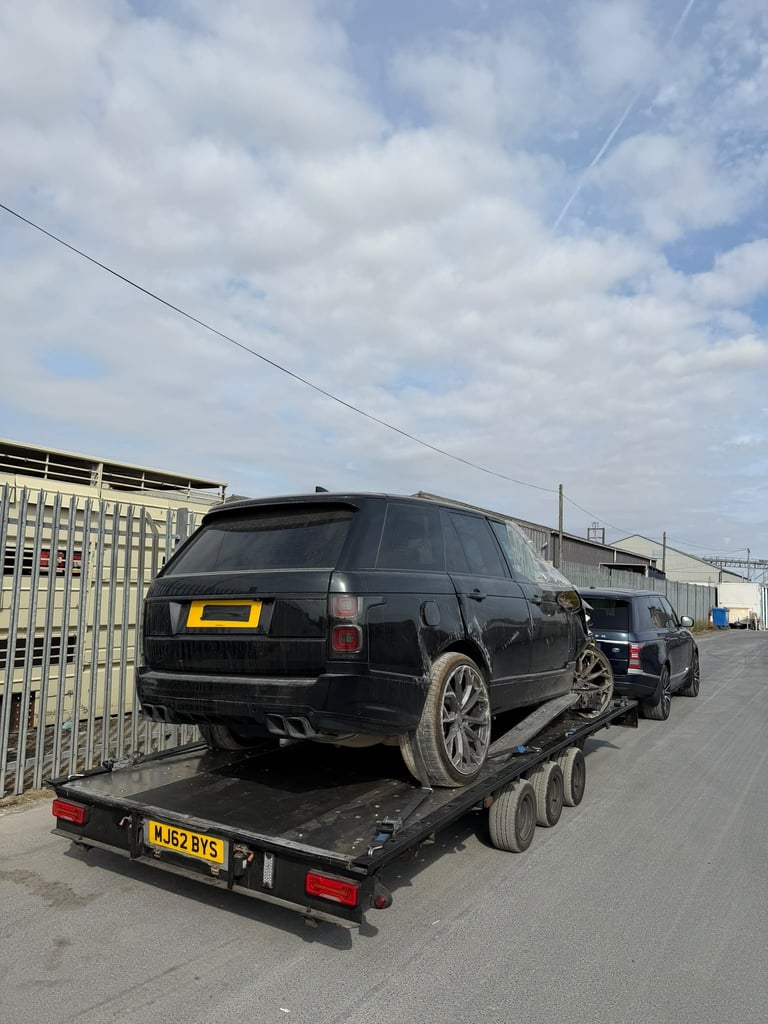 Black Range Rover loaded on a flatbed tow truck in an industrial lot