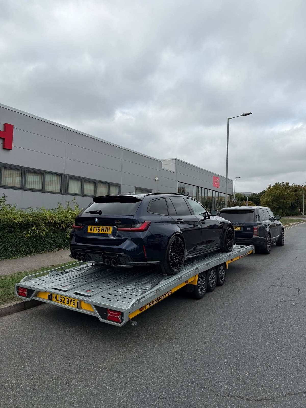 Dark blue BMW car being transported on a yellow and black car carrier trailer in an industrial parking lot