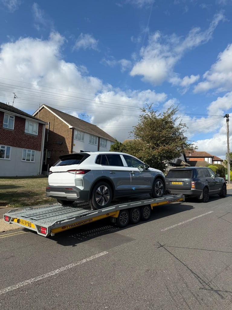 White electric vehicle being towed on a flatbed trailer in a residential street with houses in background