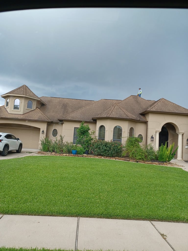Large beige stucco house with clay tile roof, arched entry, attached garage, manicured lawn, and landscaped front garden under cloudy sky