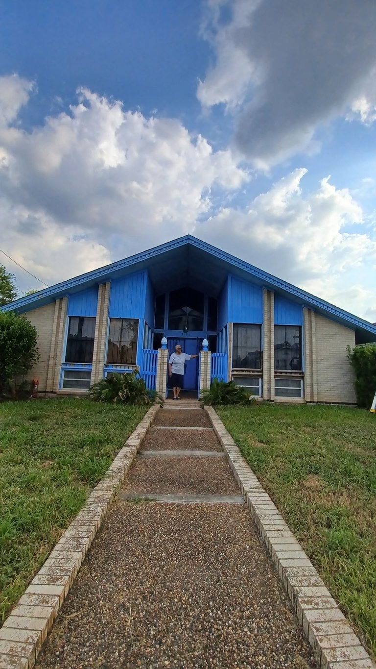 A blue and white residential house with a gabled roof and brick pathway leading to the front entrance, set against a partly cloudy sky
