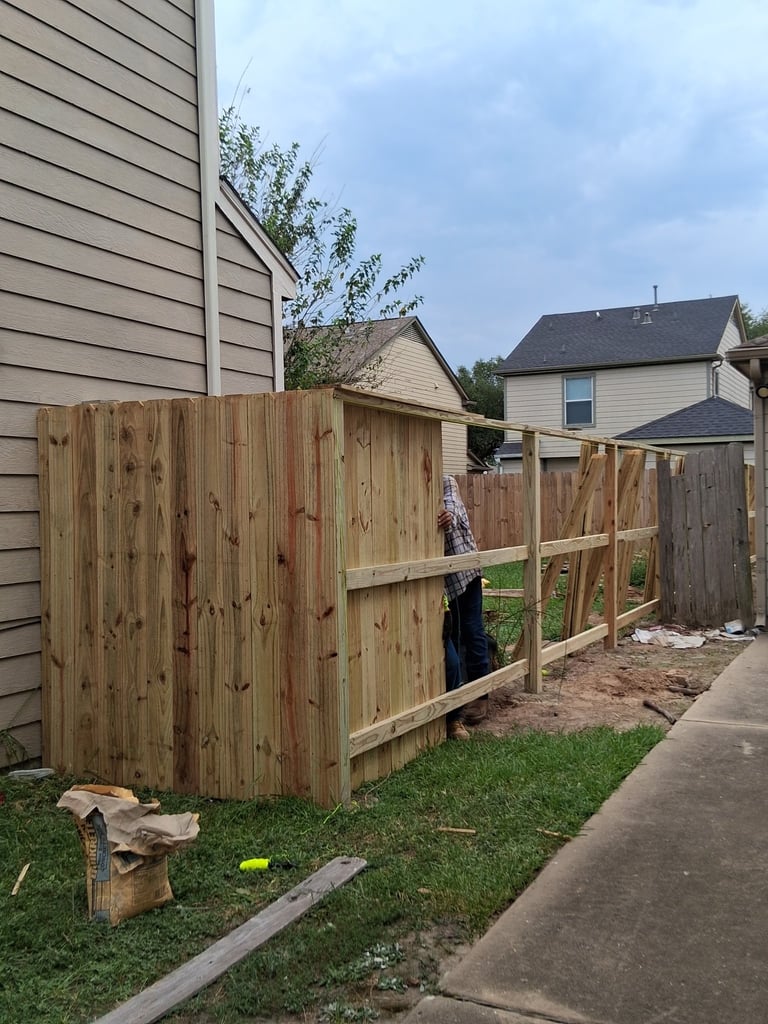Wooden fence with corner brace under construction in residential backyard with houses and grass visible