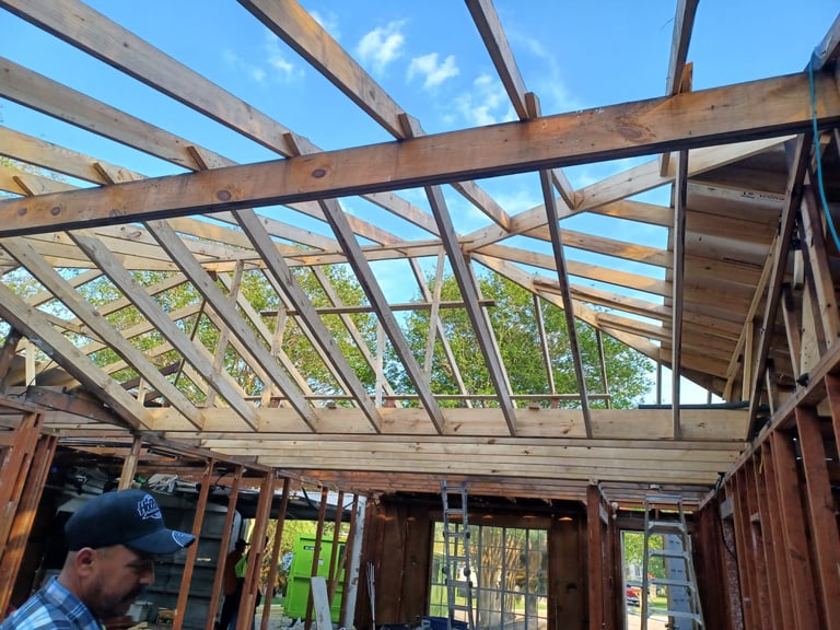 Interior view of the rebuilt home showing fresh wooden beam framing and a brand-new exposed roof structure with clear sky visible