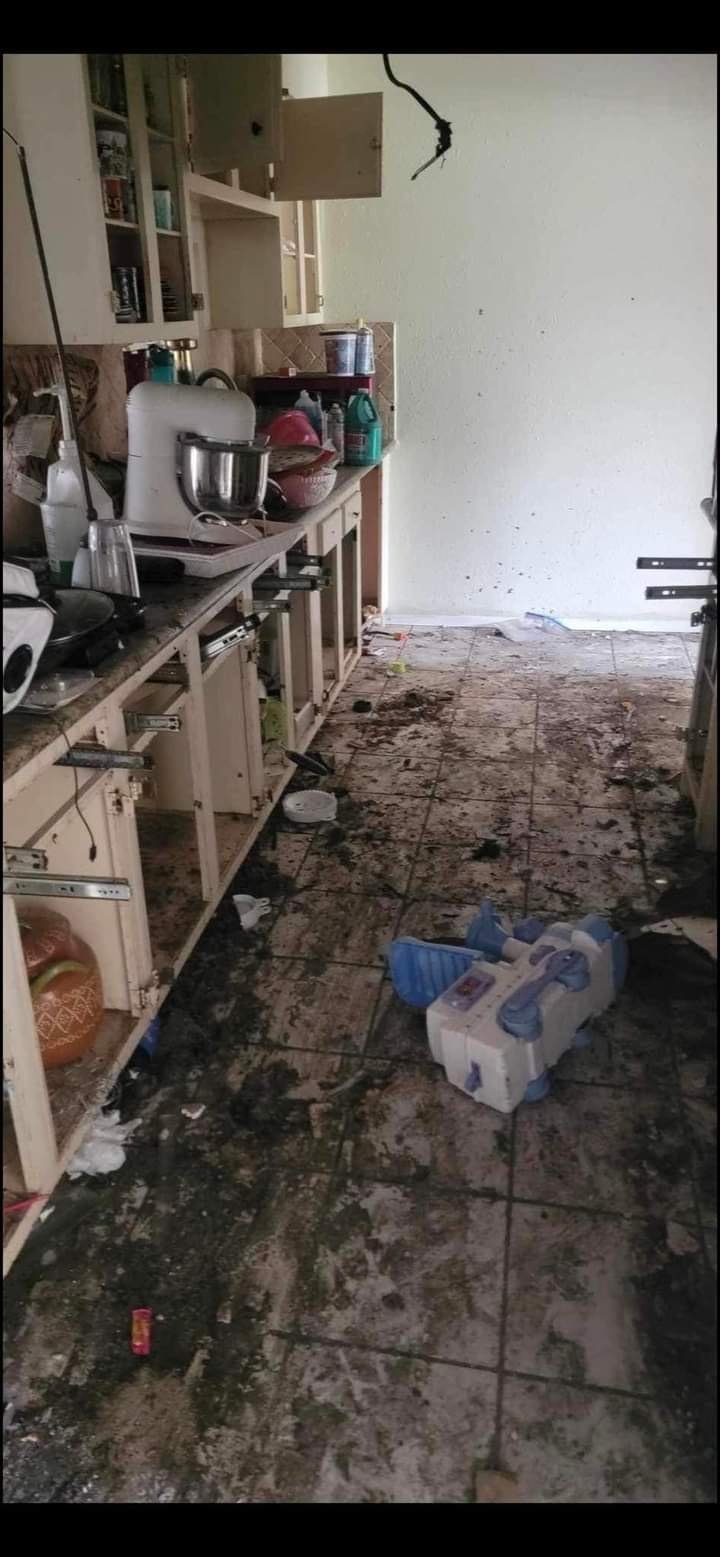 Before: Kitchen floor covered in mold and grime, with cluttered cabinets and appliances along the side wall