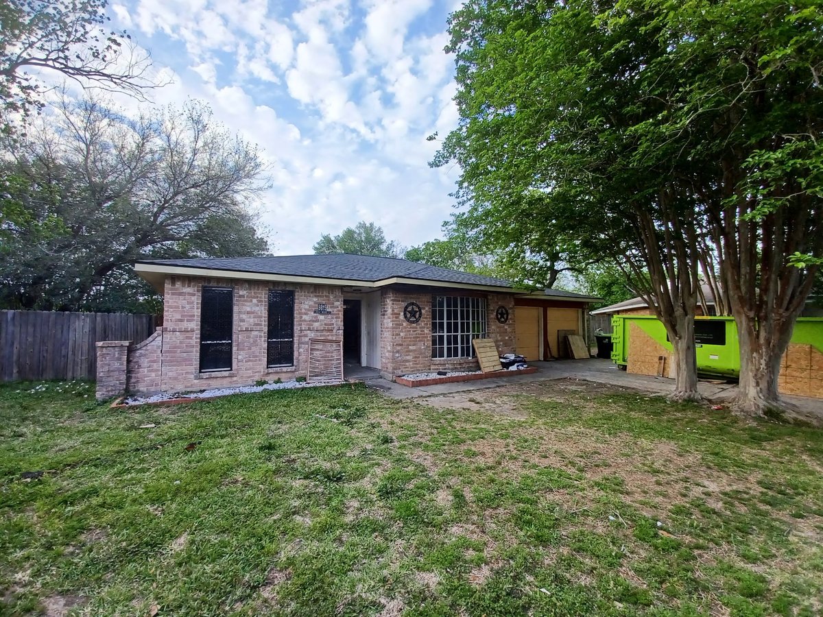 After: Single-story brick house with new roof, covered porch, and green lawn — completed fire restoration project