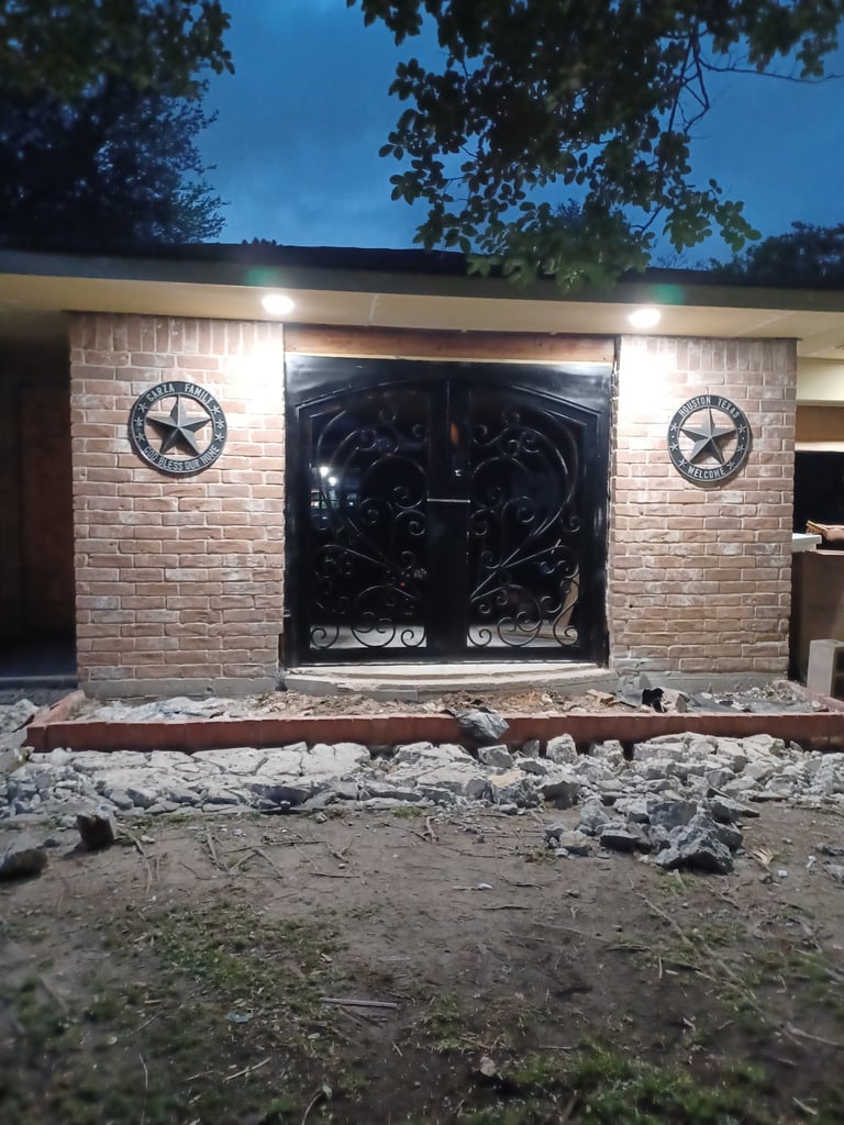 Modern garage with ornate black metal doors, brick facade, Texas star decorations, and landscape lighting at dusk