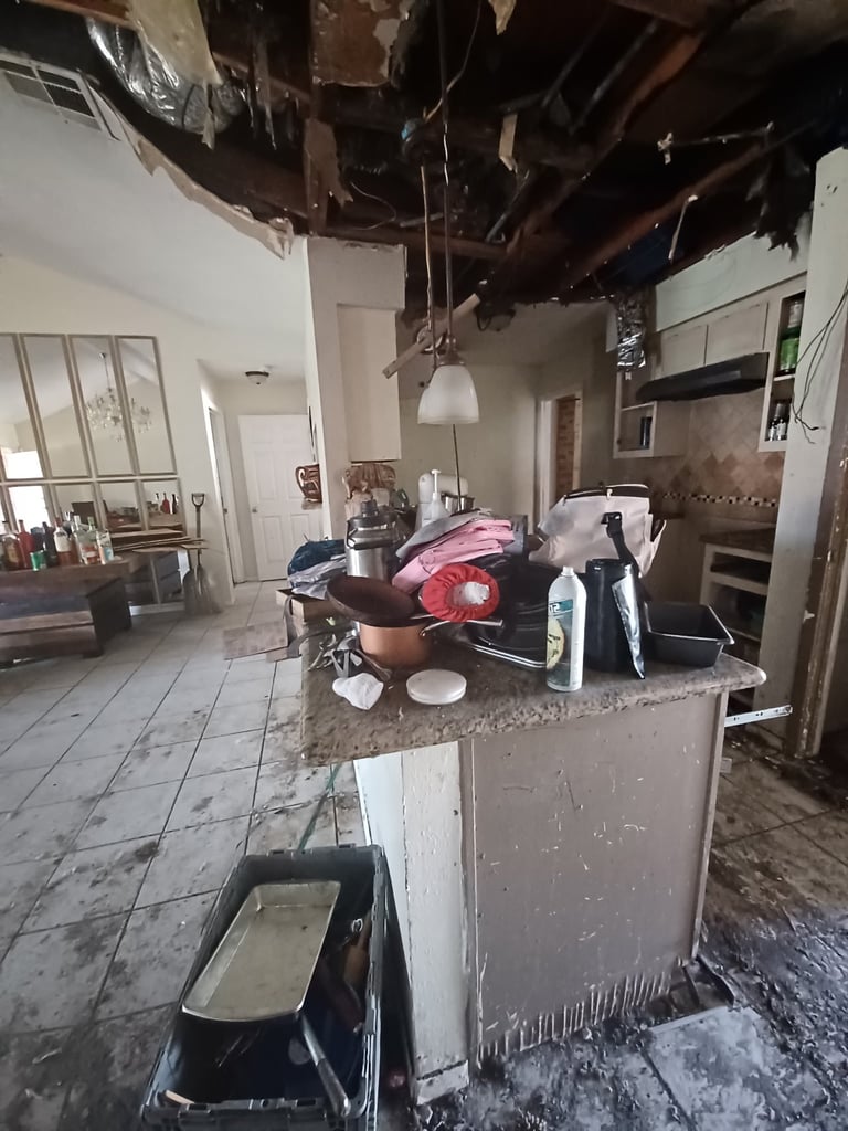 Before: Fire-damaged kitchen interior with debris on island counter, exposed ceiling beams, and ash covering surfaces