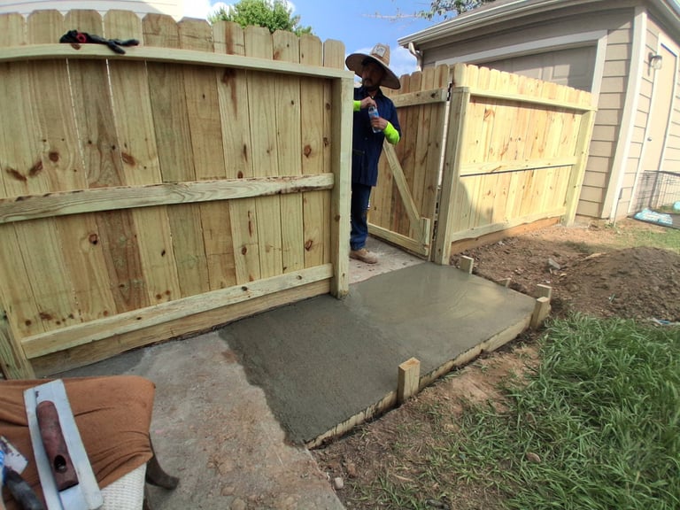Worker in blue shirt installing wooden fence gate next to concrete pad in backyard