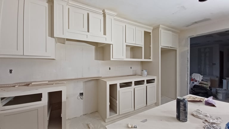 Kitchen under renovation with white cabinet frames, open wall cavities, and construction materials scattered on counter and floor