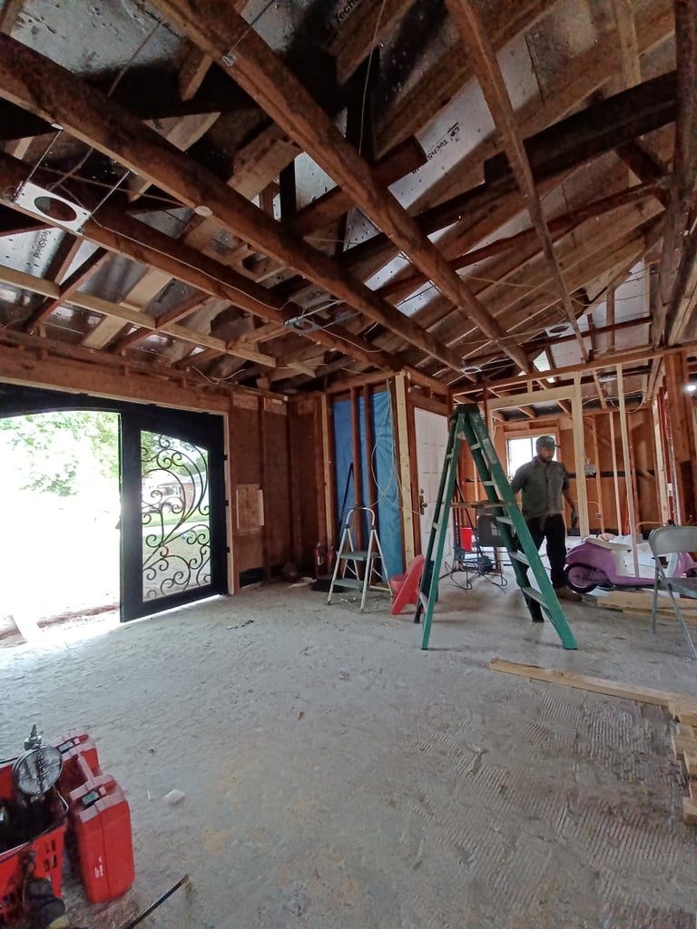 Interior of home under construction with exposed wooden framing, ladders, and tools on concrete floor