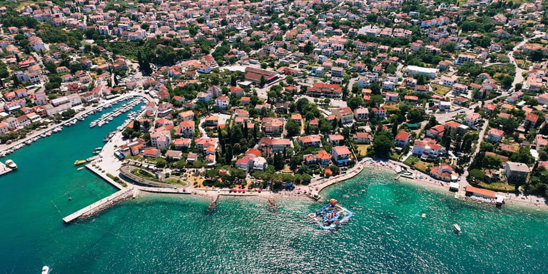 Zračni pogled na Malinsku — tirkizna voda, bijeli gat i terakota kuće među zelenilom