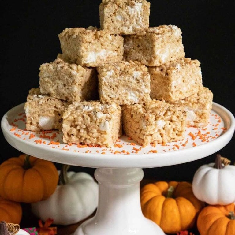 Stack of Rice Krispie treats on a white cake stand with fall pumpkin and gourd decorations on a black background