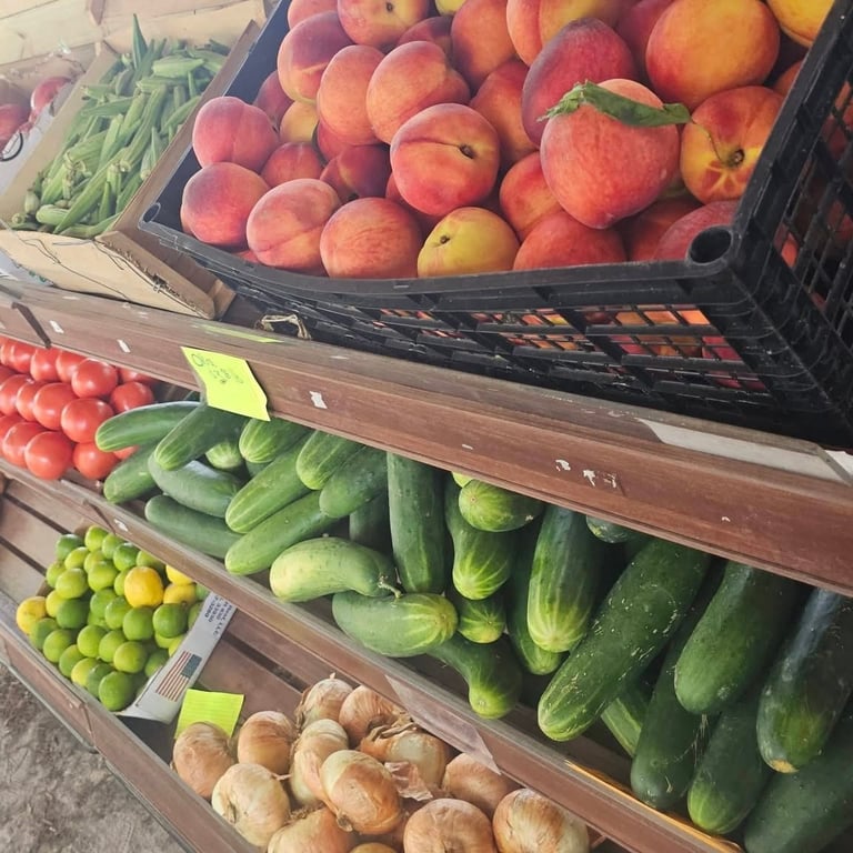 Farmers market produce display with fresh peaches, tomatoes, cucumbers, onions, and lemons arranged in wooden crates