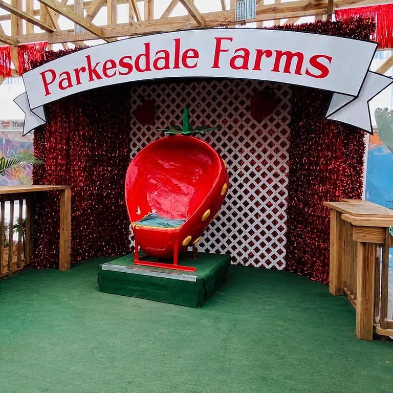 A large red apple structure inside a farm attraction booth at Parkesdale Farms with green floor and wooden gates